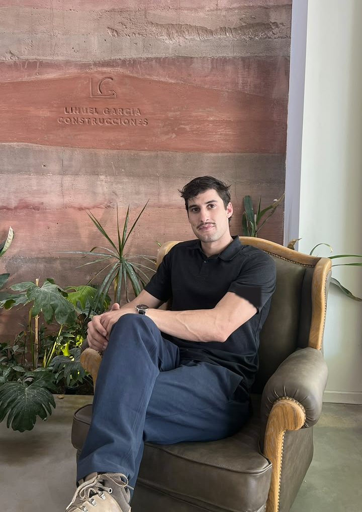 Lihuel García Tinari, sentado en un sillón frente a un muro de tierra con el logo de su estudio